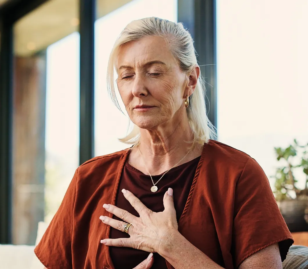 Femme aux cheveux blancs en pleine respiration consciente, main sur le cœur